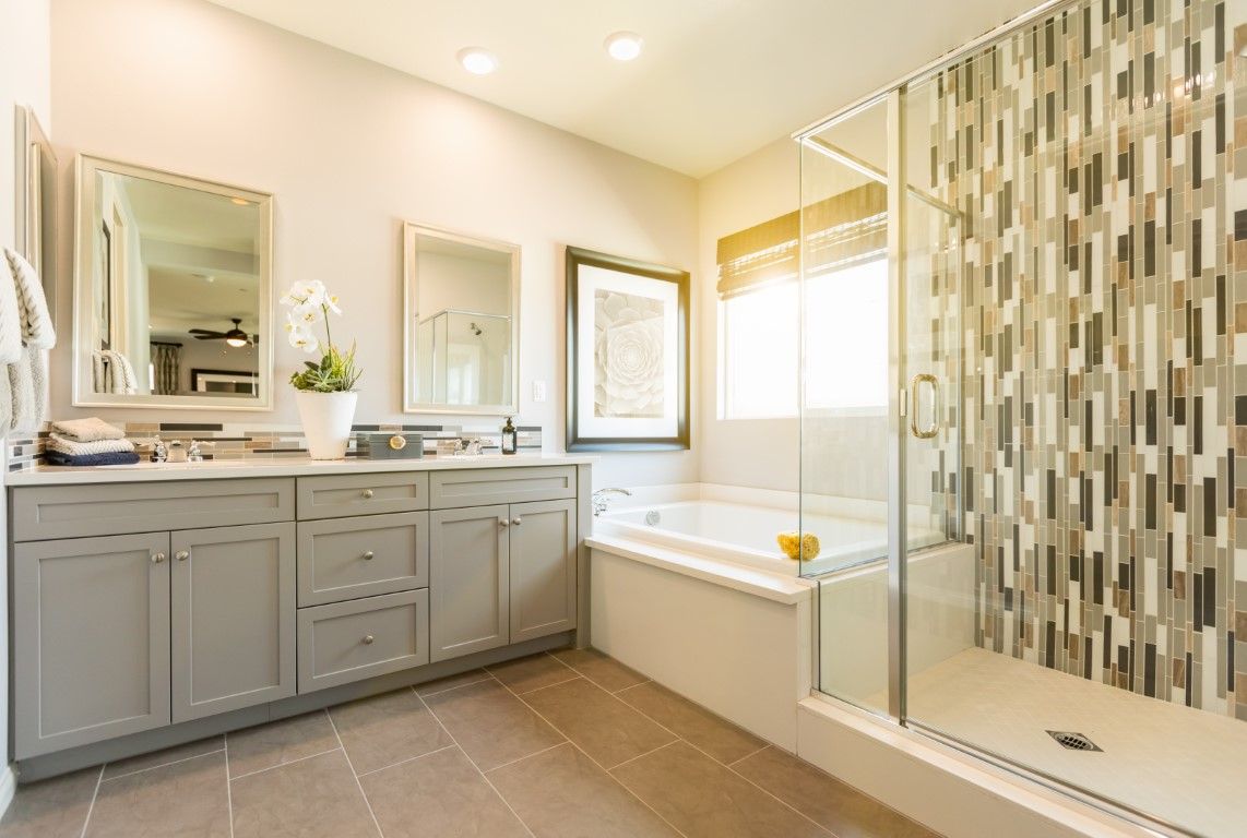 Bathroom with a grey shaker vanity, soaking tub, and a glass shower with vertical mosaic tile