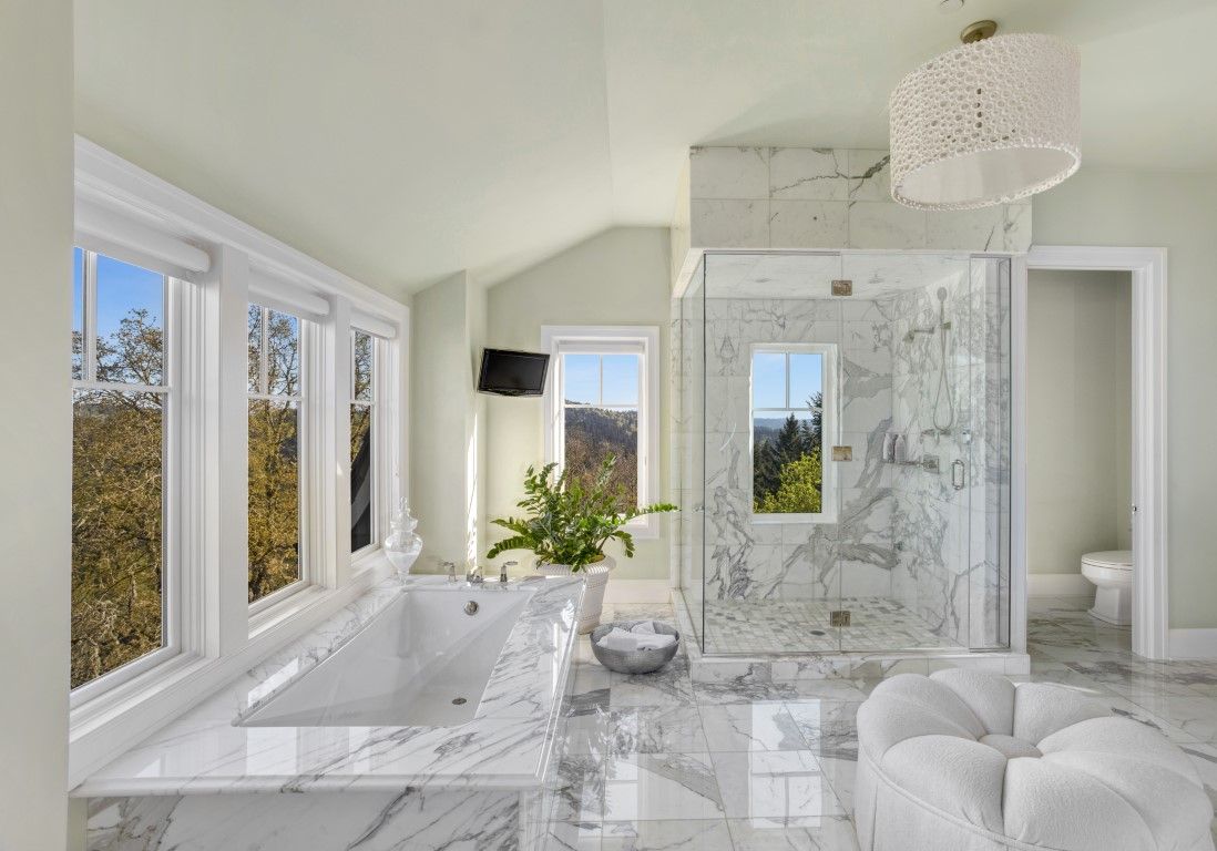 Bright bathroom with a marble-surround tub and a marble-tiled glass shower