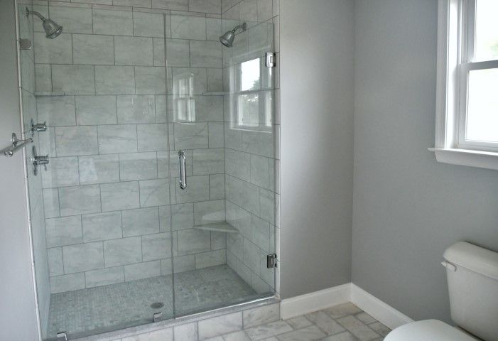 Walk-in shower with grey marble-look tile, dual showerheads, and a frameless glass door