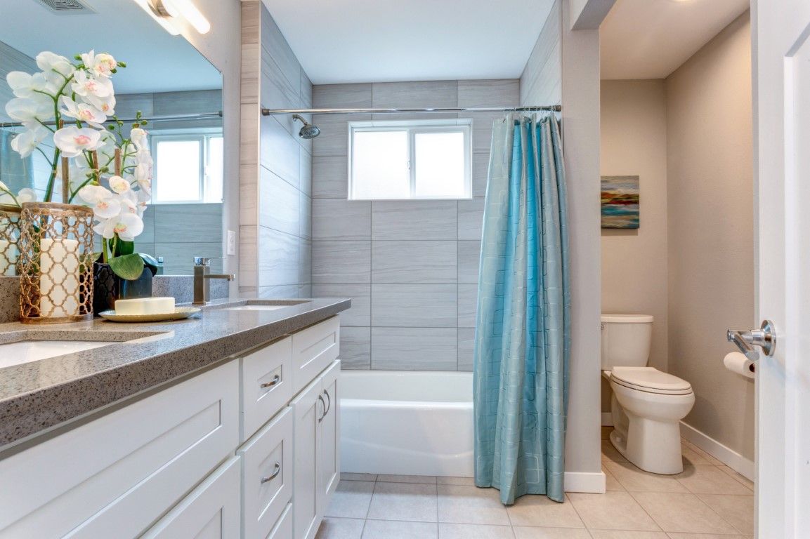 Tub and shower with large-format grey wall tile, white shaker vanity, and quartz top
